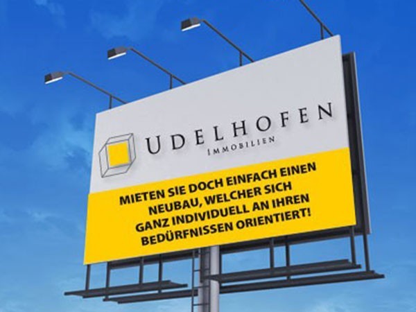 Werbetafel von Udelhofen Immobilien am blauen Himmel.