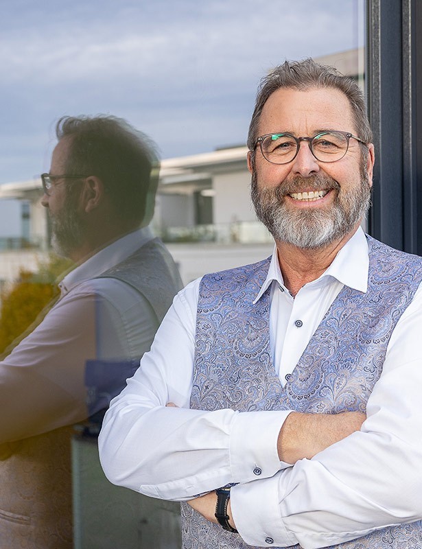 Lächelnder Mann vor einer Spiegelwand im Freien.