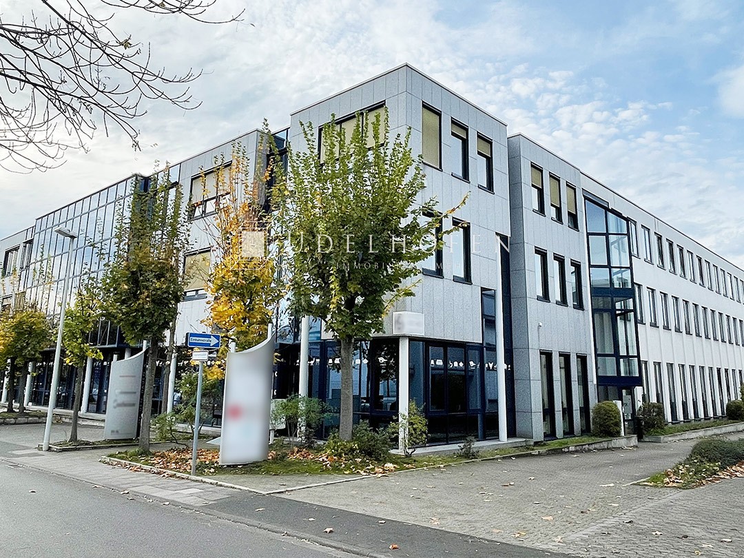 Modernes Bürogebäude mit Glasfassade und Bäumen.