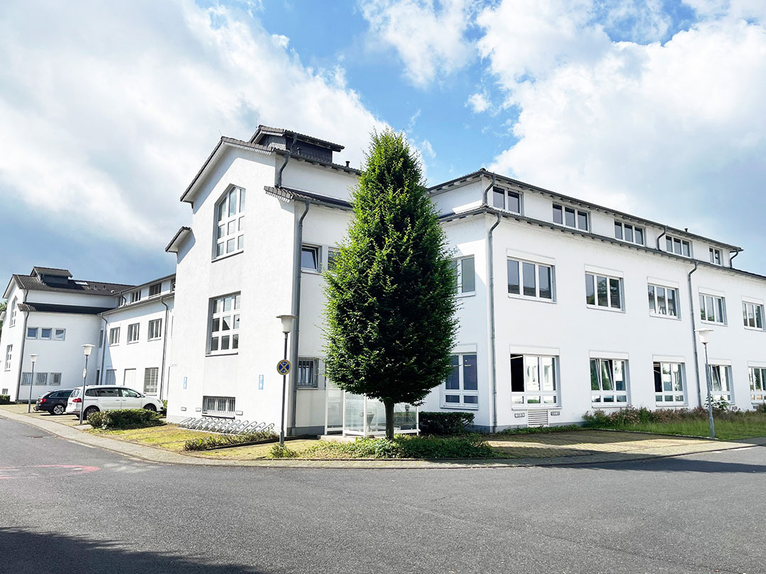 Weißes Gebäude mit Fenstern und Baum vor blauem Himmel.