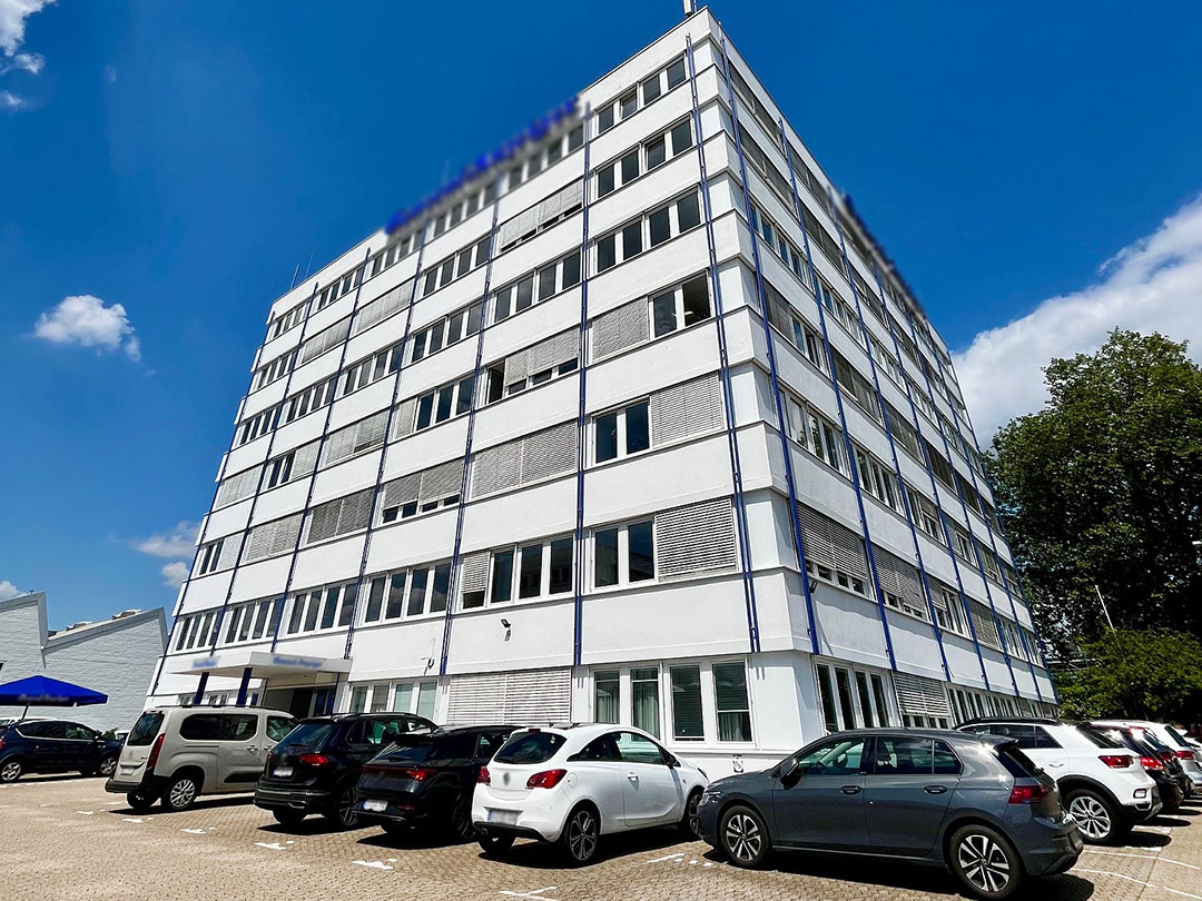 Mehrstöckiges Bürogebäude mit geparkten Autos davor.