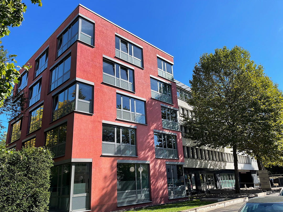 Modernes rotes Gebäude mit Bäumen davor.