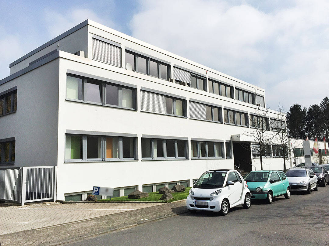 Modernes Bürogebäude mit geparkten Autos davor.