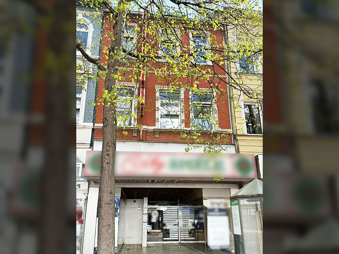 Backsteinfassade mit Baum im Vordergrund.